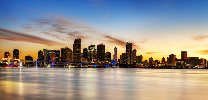 Miami city skyline panorama at dusk with urban skyscrapers over sea with reflection 