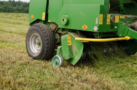 closeup special press machine equipment form round fresh hay straw bale during agricultural harvesting in field.