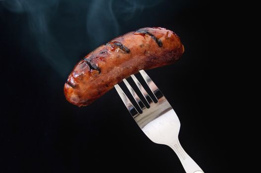 Steaming hot sausage on a fork over a black background