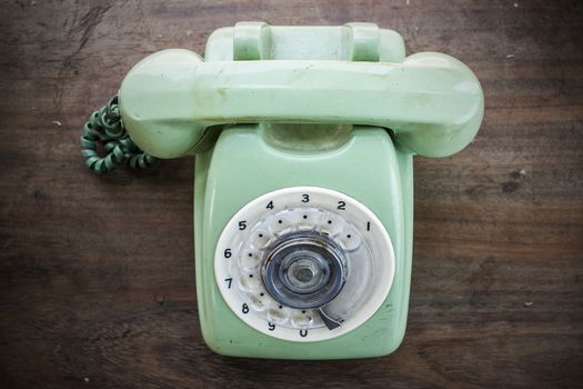 Green vintage telephone on brown wood desk background