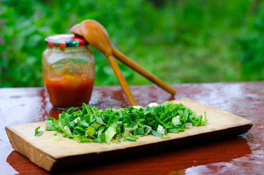  Chopped green onions on a cutting Board, on the background of two wooden spoons and cans of pepper on wet surface of the table, in nature