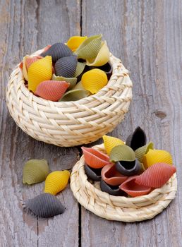 Colorful Conchiglie Pasta in Wicker Bowls isolated on Rustic Wooden background