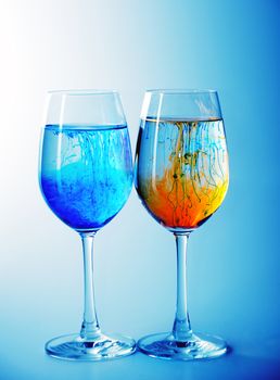Two wine glasses filled with water and spreading red,yellow  and blue ink 