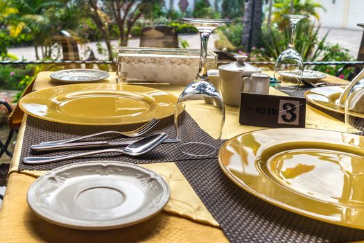 A table setup at a restaurant with plates, glasses and cutlery by the side of a window