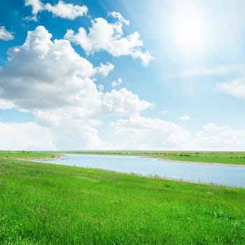 sun in cloudy sky over river with green sides