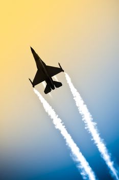 aerobatic military jet in a gradient sky leaving a smoke trail