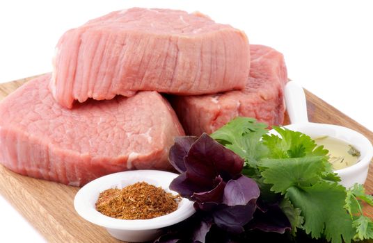 Raw Beef Steaks with Parsley and Basil, Spices and Olive Oil on Wooden Cutting Board isolated on white background