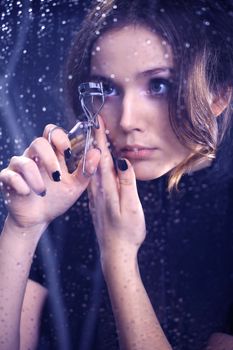 Beautiful woman eyelash curler curls lashes reviewing a reflection of the glass
