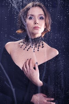 Beautiful mysterious woman dressed in black dress and lace necklace looks out the window the night