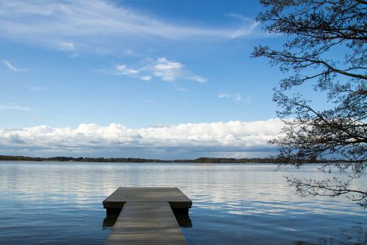 Pier and a tree under low clouds on a bright blue lake