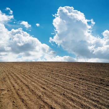 clouds in blue sky and plowed field