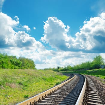 green landscape with railroad to horizon and blue sky with clouds over it