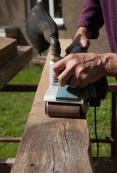 A length of wood being sanded by a power sander held in strong hands.