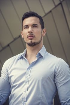 Handsome young man outside wearing shirt, looking away. Shot from below