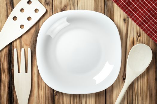 Empty white plate on table background with wooden cutlery and napkin. Top view