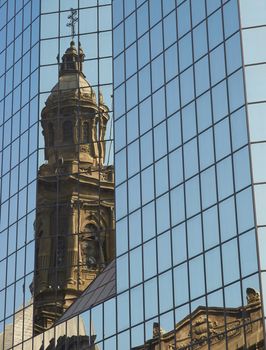 Tower of the historic Catedral Metropolitana reflected in the glass of a modern office building in the Plaza de Armas in Santiago, Chile