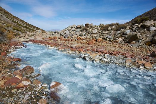 Ice cold river from the Paloma glacier running through autumn coloured vegetation in the Yerba Loca Mountain Park near Santiago in Chile