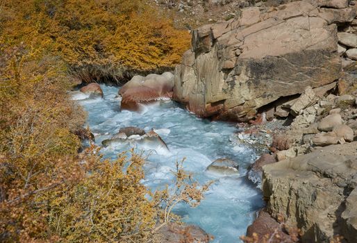 Ice cold river from the Paloma glacier running through autumn coloured vegetation in the Yerba Loca Mountain Park near Santiago in Chile