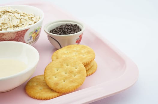 Cracker, oat, chocolate and  sweetened condensed milk placed on a pink plate.