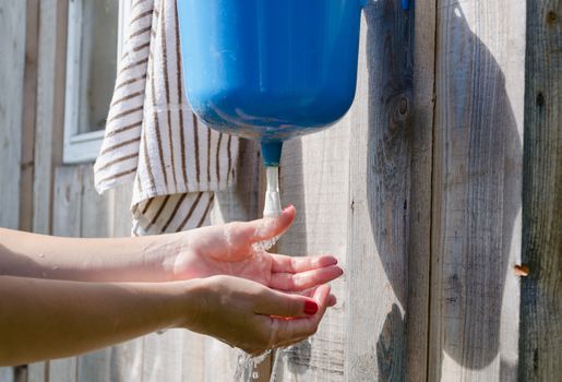 Closeup of gardener girl woman with red nails wash hands under rural plastic washer tool water.