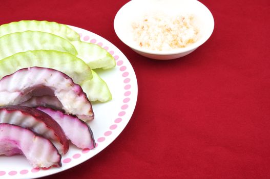 Malay apple and guava slices with salt and pepper in a plate with red background.