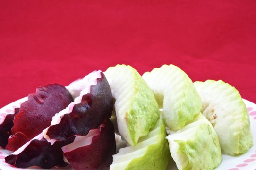 Malay apple and guava slices in a plate with red background.