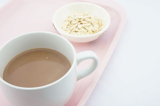 Cup of cocoa and oats in a small bowl placed on pink tray with white background.
