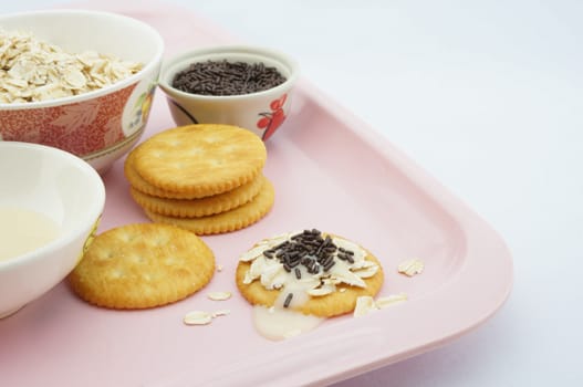 Cracker, oat, chocolate and  sweetened condensed milk placed on a pink plate.