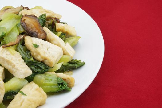 Stir-fried brassica with shitake mushrooms and tofu on a red background.