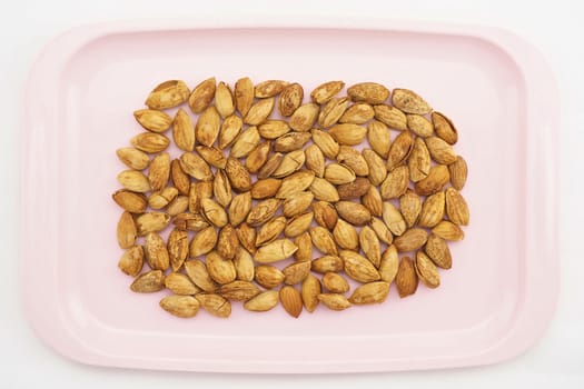 Almond with hull placed on pink tray with white background.