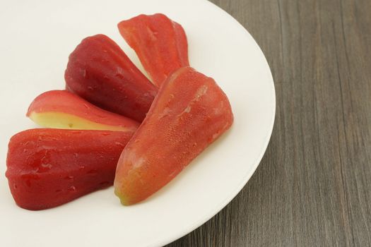 Fresh and cold rose apple put in plate on dark brown wood background.