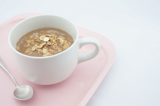 Cup of coco with oats placed on pink tray with white background.