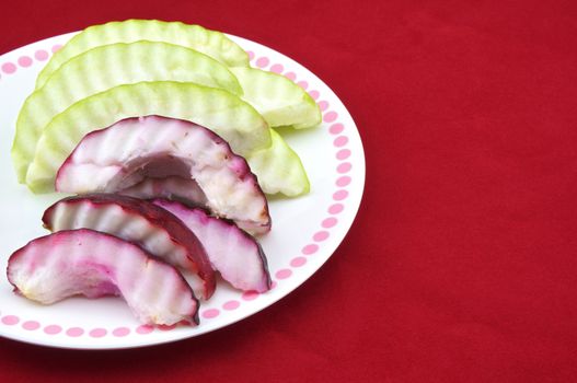 Malay apple and guava slices in a plate with red background.