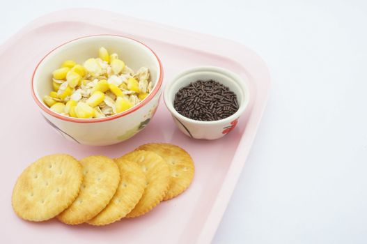 Mix corn, oats and sweetened condensed milk with chocolate placed on pink tray with white background.