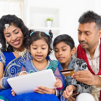 Indian Asian family using digital tablet pc computer online shopping with credit card at home. India family living lifestyle. Happy smiling parents and children.