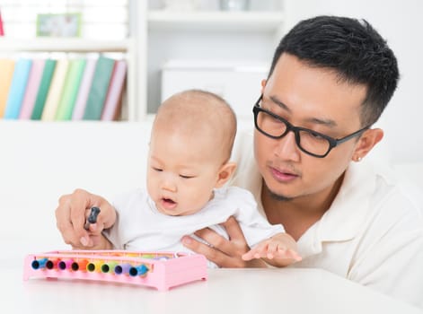 Asian family lifestyle at home. Father playing music instrument with baby. Sound development concept.