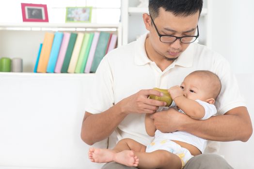 Asian family lifestyle at home. Father bottle feeding baby fruits puree.