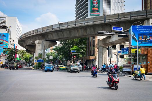 BANGKOK, THAILAND - 21 NOV 2013: Motorbikes and cars pass big crossroads street with skytrain track on background
