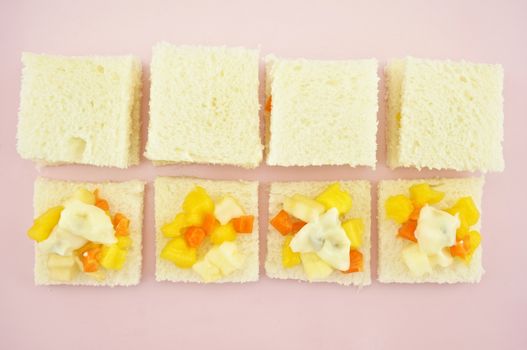 Carrot, Mango, apple and cucumber sliced put on small bread with cream salad in row for make sandwich on pink tray.