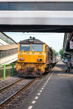 Dong Mueang, Thailand - 21 Nov 2013: Yellow locomotive with train arrives at railway station with people on outdoor platforms