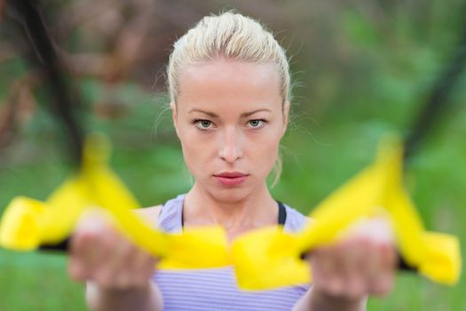 Young attractive woman does suspension training with fitness straps outdoors in the nature.