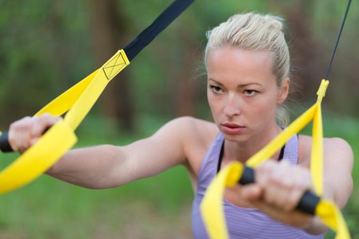 Young attractive woman does suspension training with fitness straps outdoors in the nature.