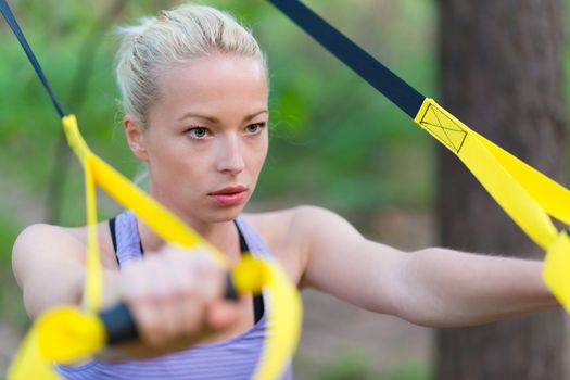 Young attractive woman does suspension training with fitness straps outdoors in the nature.