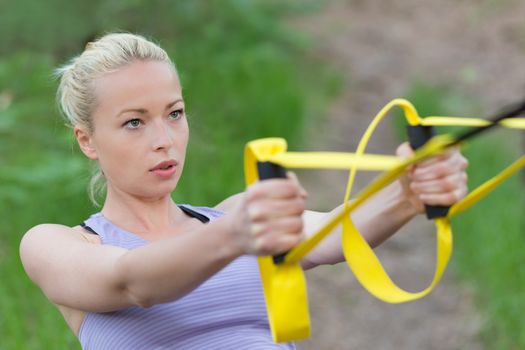 Young attractive woman does suspension training with fitness straps outdoors in the nature.