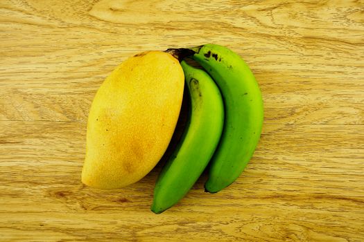 Big yellow mango or Mangifera indica and green cavendish banana put on wood background.