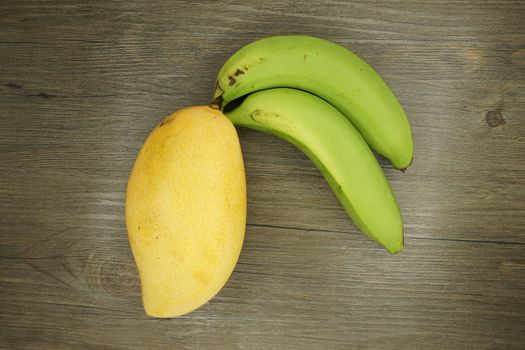 Big yellow mango or Mangifera indica and green cavendish banana put on wood background.