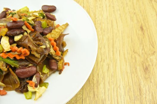 Fired thin noodles with soy sauce vegetarian in plate placed on brown wood background