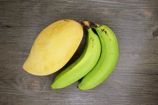 Big yellow mango or Mangifera indica and green cavendish banana put on wood background.