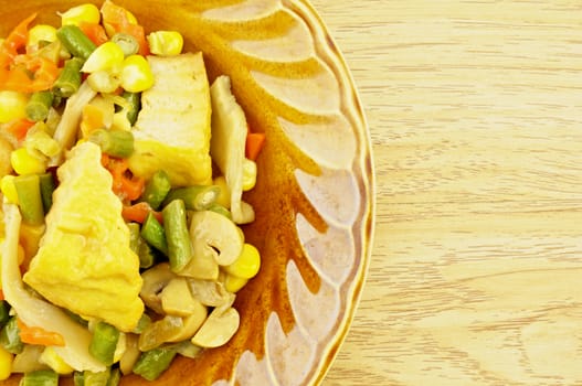 Tofu fried carrot, champignon mushroom, corn, vigna unguiculata sesquipedalis on dish with wood background.