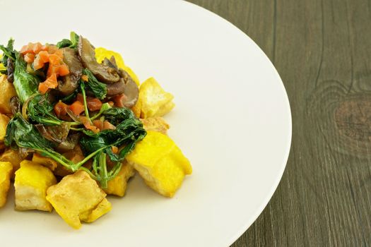 Tofo fried with carrot, basil and mushroom in plate on wood background.